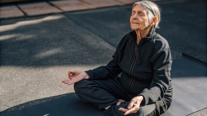 An elderly person sits crosslegged on a yoga mat meditating with eyes closed