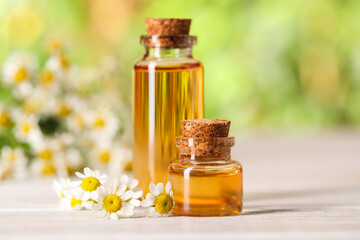 Canvas Print - Bottles of essential oil and chamomile flowers on white wooden table against blurred background, closeup