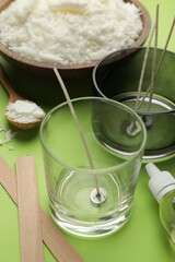 Wall Mural - Making homemade candles. Soy wax in bowl, jars with stabilizers, wicks and essential oil on green background, closeup