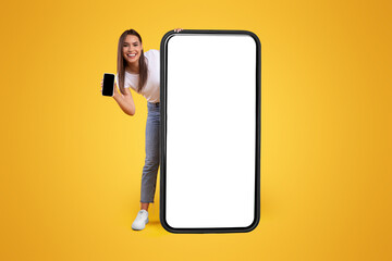 Wall Mural - full body length of cheerful woman peeking out standing behind big smartphone with white blank scree