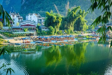 Reflections of serene bamboo forests and traditional boats at a riverside village during sunrise in tranquil nature