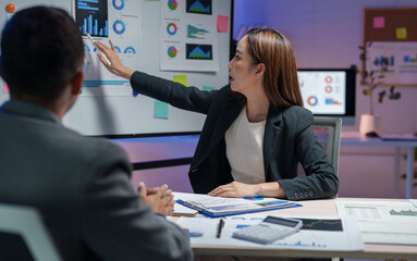 Sticker - Businesswoman presenting data analysis on a digital screen in a modern office setting. Colleagues engaged in discussion with charts and graphs. Professional atmosphere with focus on teamwork