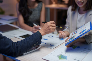 Wall Mural - Business team collaborating in an office at night, analyzing charts and graphs, discussing financial strategies, and planning projects to meet deadlines and achieve growth