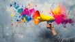 © a muh sakaria - Hand holds megaphone, colorful paint splatters, gray wall background