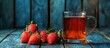 © Rufat - Glass of amber tea beside fresh red strawberries on a rustic blue wooden background creating a refreshing vibrant contrast and inviting atmosphere