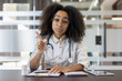 © Tetiana - Portrait of a serious young African American female doctor sitting in a hospital office at a table with documents, talking and gesturing to the camera