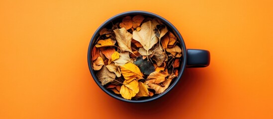 Leinwandbilder - Dried autumn leaves in a black cup on vibrant orange background. Flat lay top view with warm earthy tones and ample copy space for fall concept.