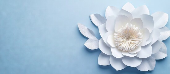 Leinwandbilder - Delicate handmade white paper flower with intricate petals and a soft beige center on a light blue background, positioned in the right foreground.