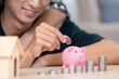 © itchaznong - LGBTQ couple saving coins in a pink piggy bank at home, promoting financial literacy and savings