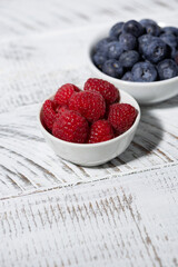 Wall Mural - fresh blueberries and raspberries in a bowl on white table, vertical