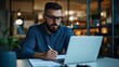 © Bayu - Focused man works late, laptop, notes, office