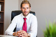 © Minerva Studio - Confident businessman sitting at desk in modern office