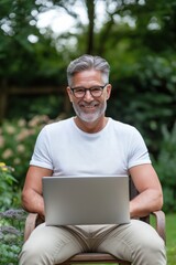 Wall Mural - A man with a laptop is sitting on a chair in a garden. He is smiling and he is enjoying his time