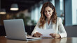 © halo - A female business professional is working on a laptop and reading documents in a modern office