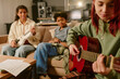 © AnnaStills - Medium close up of beautiful teen girl playing acoustic guitar while her friends watching, focus on guitar