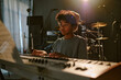 © AnnaStills - Tired teen boy looking at papers with notes while playing keyboard at dimly lit studio