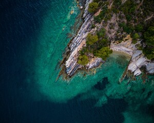 Wall Mural - An aerial view of a rocky coastline with vibrant turquoise waters and lush greenery.