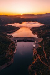 Wall Mural - Dam landscape at sunset with fog in mountains for energy or water reservoir