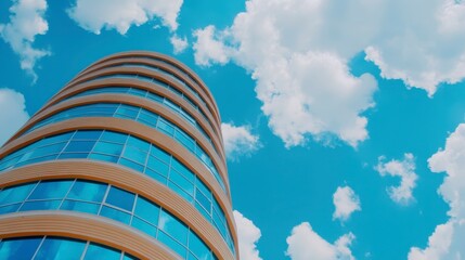 Wall Mural - Low angle view of a modern, cylindrical office building with light beige wooden panels and many transparent glass windows, set against a vibrant blue