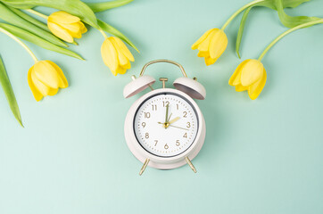 Alarm clock with yellow tulip flowers, switch to daylight saving time in spring, summer time changeover