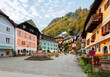 © AaronPlayStation - Scenic view of the old town square of Hallstatt, with a statue in the center, traditional colorful houses around the paved square, and fall mountains in background in Salzkammergut region of Austria