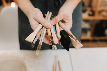 Poster - Potter holds craft instruments for clay sculpting. Wooden craft tools for molding ceramic crockery.