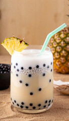 Wall Mural - A tropical coconut bubble tea with black pearls, garnished with a pineapple slice, on a sandy beach-inspired background.