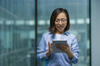 © Liubomir - Successful joyful Asian woman inside office at workplace holding tablet computer in hands. Businesswoman using online application, reading email.