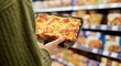© Tati - Person holding prepackaged lasagna in supermarket frozen food aisle