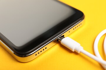 Wall Mural - USB charge cable connected to smartphone on orange background, closeup