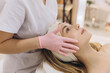 © anatoliycherkas - Beautician wearing pink gloves applying moisturizing cream on young woman face lying on a massage table at beauty salon
