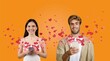 © Prostock-studio - A cheerful couple stands together, smiling and using their smartphones to send affectionate messages. Heart graphics surround them, highlighting their love during St. Valentine's Day celebrations.