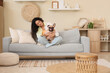 © Pixel-Shot - Happy young African-American woman with cute French bulldog sitting on sofa in living room