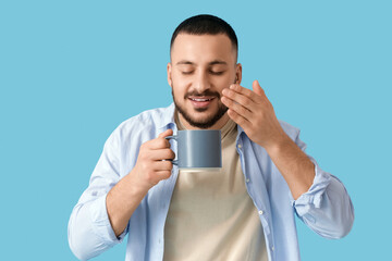 Wall Mural - Young man with ceramic cup on blue background