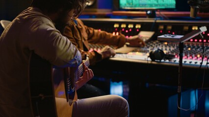 Leinwandbilder - Creative musician singing guitar in professional studio control room, recording his tracks with producer. Singer songwriter composing a new song for his album, editing tunes on console. Camera A.