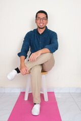 Wall Mural - A man sitting on the chair with one leg crossed showing happy face expression