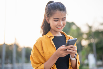 Wall Mural - Smiling young Asian woman using smartphone in urban city checking apps mobile outdoors