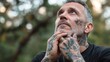 © atipong - Thoughtful Man with Tattoos Gazing Outdoors Amidst Nature