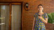 © Mauricio Abarca - Modern Lifestyle: A portrait of a smiling woman holding a phone, she is standing against a brick wall, embodying contemporary life. The sun gently illuminates the scene.