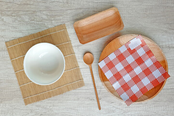 Food mockup flat lay composition. Empty plastic white bowl on bamboo mat, wooden plate, tray, spoon with checkered paper napkin on wooden table. Japanese style template. Top view rustic table setting.