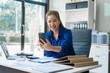 © Phushutter - Attractive Asian businesswoman in formal business attire is working at her desk with a laptop and mobile phone, focusing on corporate law, contracts, compliance, and law firm marketing strategies.