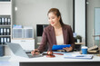 © Phushutter - Attractive Asian businesswoman in formal business attire is working at her desk with a laptop and mobile phone, focusing on corporate law, contracts, compliance, and law firm marketing strategies.
