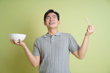 Young Asian man holding a bowl on green background