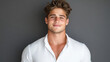 © Panupan - Confident young man smiling in white shirt against gray background, exuding charm and positivity. His stylish hair adds to overall appeal of portrait