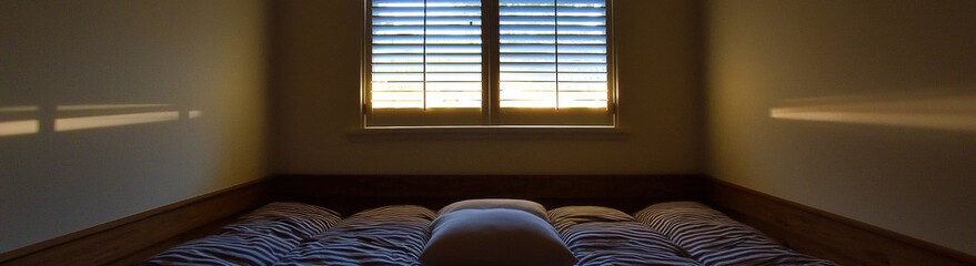 Poster - cozy bedroom with low bed, striped bedding, and single pillow, illuminated by soft sunlight streaming through wooden window shutters