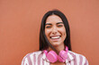 © Sabrina - Portrait of native american woman smiling on camera with city wall in background - Indigenous girl with headphone outdoor