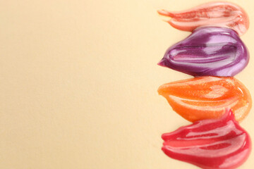 Wall Mural - Samples of different lipglosses on beige background, closeup. Space for text