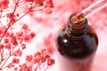 Wall Mural - Dripping serum from pipette into bottle and gypsophila flowers on pink background, closeup