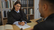 © Krakenimages.com - Female judge in black robe listening to male client at desk in office interior with bookshelves and legal documents visible, creating a professional courtroom setting