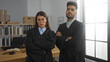 © Krakenimages.com - Woman and man standing together in an office with arms crossed, wearing judge robes, in a serious workplace setting